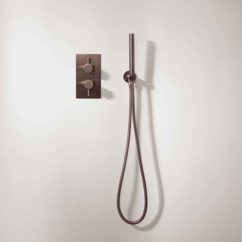 Close up product lifestyle image of the JTP Vos Brushed Bronze Single Outlet Concealed Shower Valve mounted adjacent to a pencil handset shower